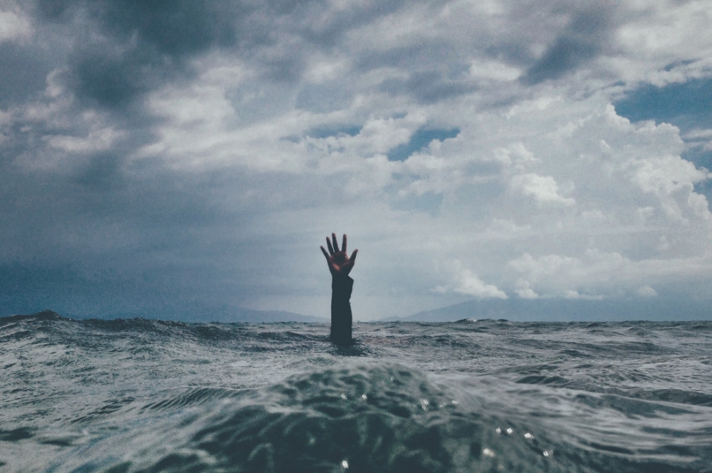 A human hand reaches above turbulent waves of water.